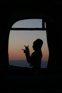 Silhouette man standing by window at sunset
