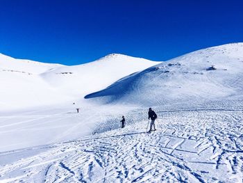People skiing on snowcapped mountain against clear blue sky