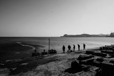 Silhouette people standing on beach against clear sky