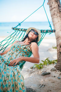 Woman wearing hat relaxing on hammock at beach