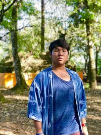 Portrait of young man standing against trees in forest