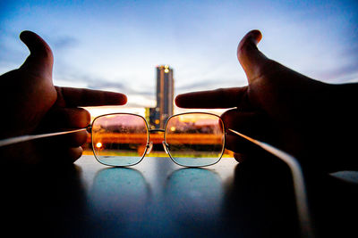 Close-up of hand holding eyeglasses against sky