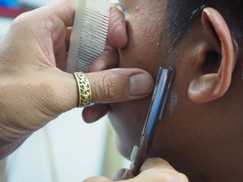 Cropped hands of barber cutting customer beard in salon