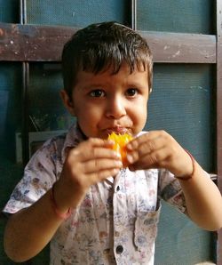 Portrait of boy eating food while sitting against door at home