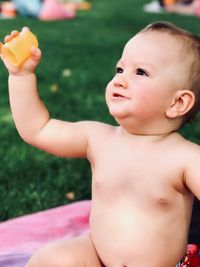 Naked baby boy holding toy while sitting in park