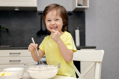 Little boy kneading dough with a whisk in the kitchen and smiling. time with children at home.