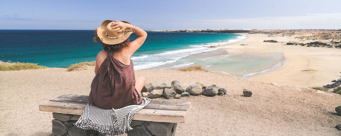 Rear view of woman with hat sitting at beach