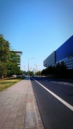 Empty road by buildings against clear blue sky