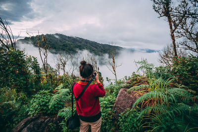 Rear view of man standing on mountain against sky