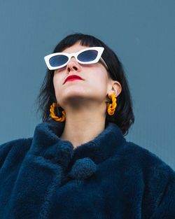 From below of unemotional female with red lips and in fancy outfit standing against metal wall in city and looking up with stylish sunglasses