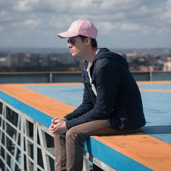 Side view of young man sitting against sky