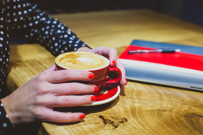 Cropped image of hand holding coffee cup on table