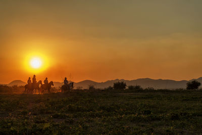 Silhouette people on field against orange sky