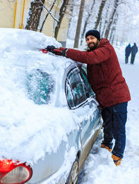 Man standing on snow covered car during winter