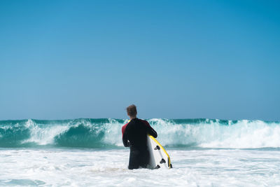 Rear view of man looking at sea against clear sky