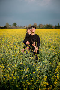 Rear view of woman standing amidst yellow flowering plants on field against sky