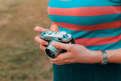 Midsection of woman holding camera while standing outdoors