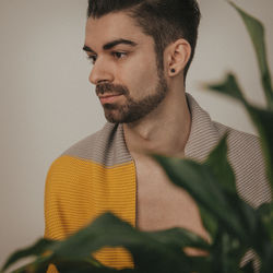 Portrait of a young man looking away, behind a plant.