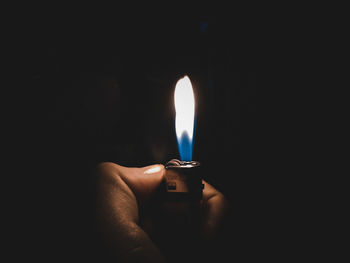 Close-up of hand holding burning candle in darkroom