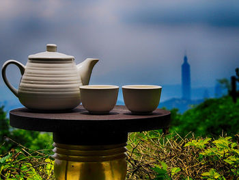 Cups with teapot on table against sky