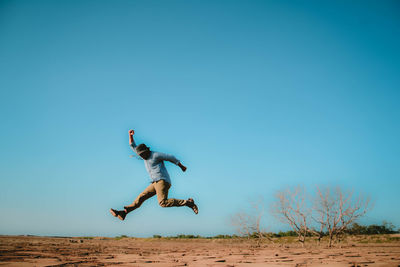 Man jumping on field against sky