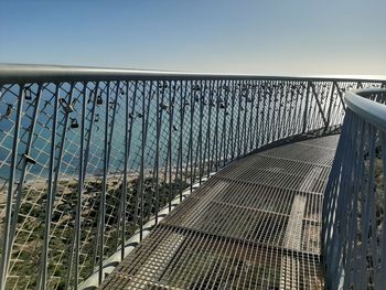 Metal fence by bridge against sky