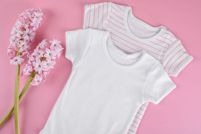 Mockup of cotton baby girl bodysuit with pink hyacinth flowers flat lay layout on pink background