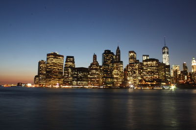 Illuminated buildings in city against clear sky at night