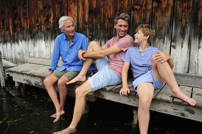 Boy sitting with grandfather and father together on jetty in summer