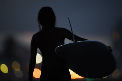 Rear view of silhouette woman with surfboard at beach during night