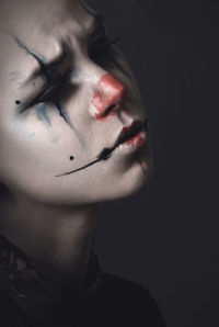 Close-up of young woman with clown make-up over black background