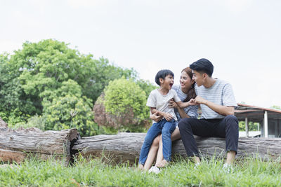 Side view of young man sitting on tree trunk