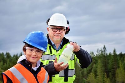 Portrait of smiling grandfather and grandson wearing hardhats against cloudy sky