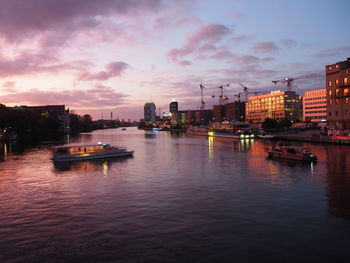 Boats in river against buildings in city at sunset