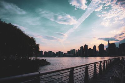 Silhouette buildings by river against sky during sunset