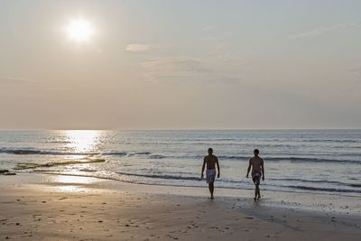 Man walking with son on shore at beach during sunset