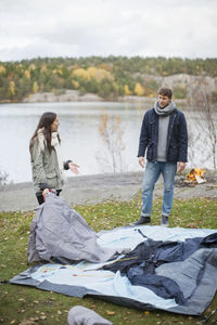 Couple communicating while setting up tent on lakeshore