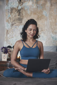 Full length of woman using laptop while sitting on bed at home