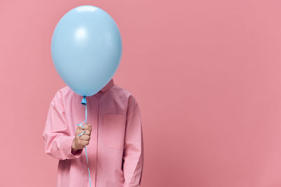 Boy covering face with blue balloon against pink background