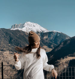 Young woman standing on snowcapped mountain against sky