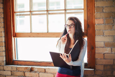 Thoughtful woman with book standing by window