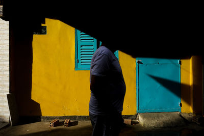 Rear view of man standing against yellow wall