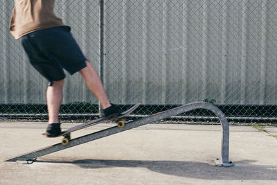 Low section of man skateboarding on metal against fence