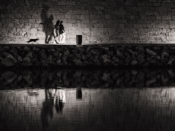 Blurred motion of women walking on footpath with reflection in lake at night