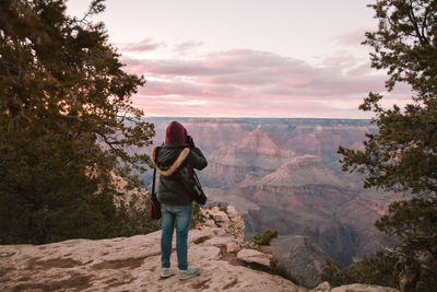 Rear view of woman standing on rock against sky