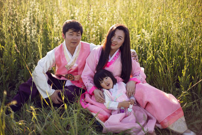 Korean family with their daughter sit in a field in the grass at sunset in summer