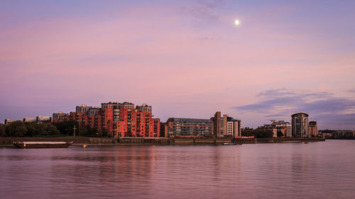 Buildings by river against sky at dusk