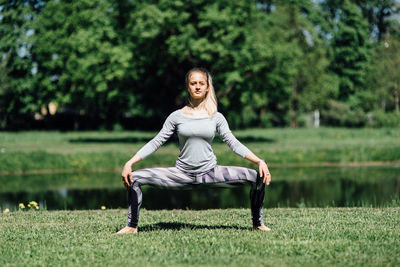 Full length of woman exercising on field by lake at park