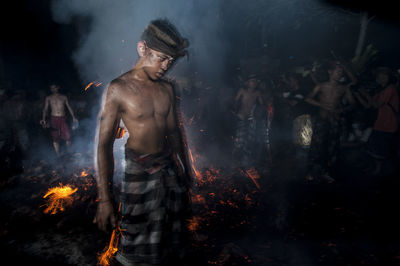 Young man standing against campfire at night