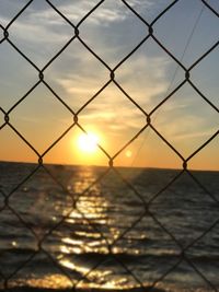 Close-up of chainlink fence against sky during sunset